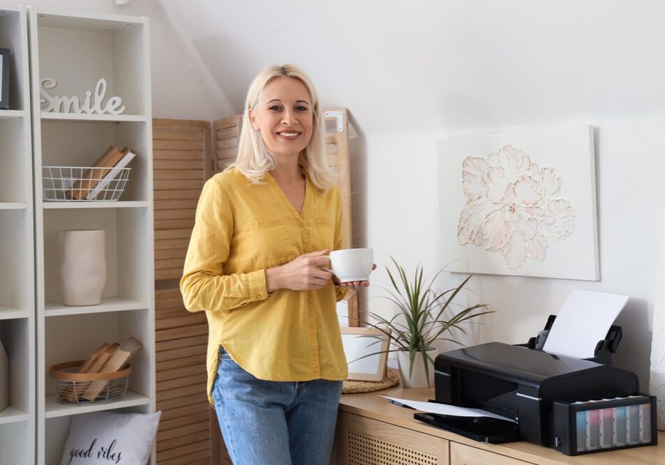 Mature,Woman,With,Cup,Of,Coffee,And,Printer,On,Commode